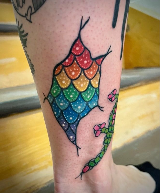 Neo traditional rainbow mermaid scales tattoo on a lower leg.